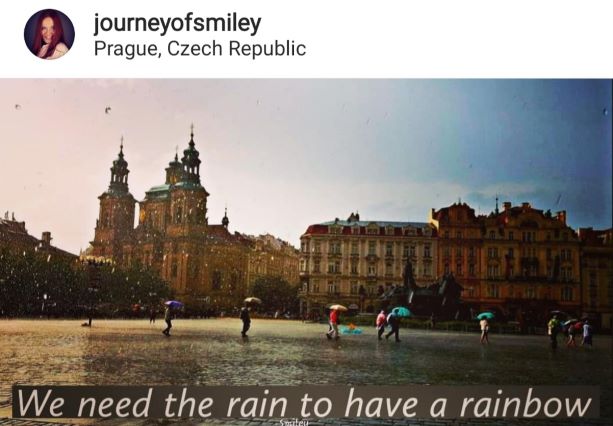 Photo of Prague main square on a rainy day, people walking with umbrellas, and  below is an inspirational quote about rainbow by Journeyofsmiley on IG