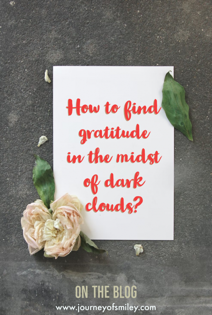 A note 'How to find gratitude in the midst of dark clouds?' on a white paper on a dark background with a rose on the paper, on Journeofsmiley Blog