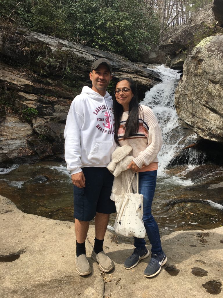 a couple, two people, a man and a woman, standing in front of a waterfall, on rocks