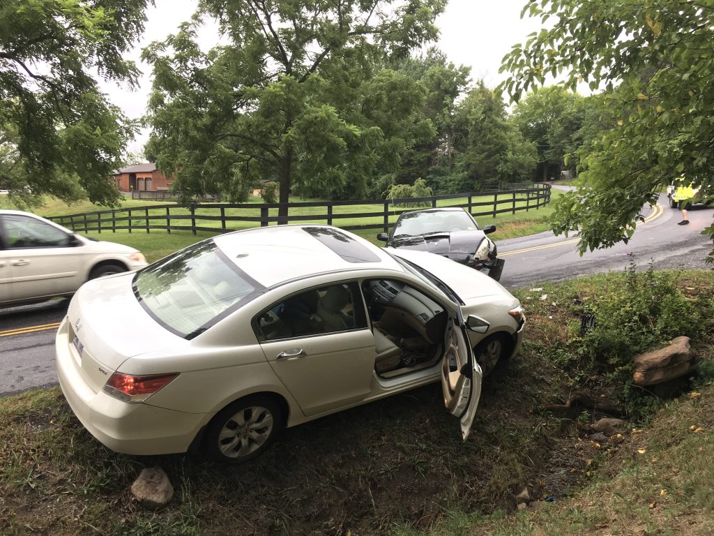 A car in ditch with open passenger doors. Two car crashed into each others on a street.