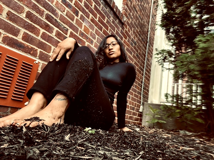 A woman sitting on woodchips next to a house on the ground. Trauma survivor and a warrior