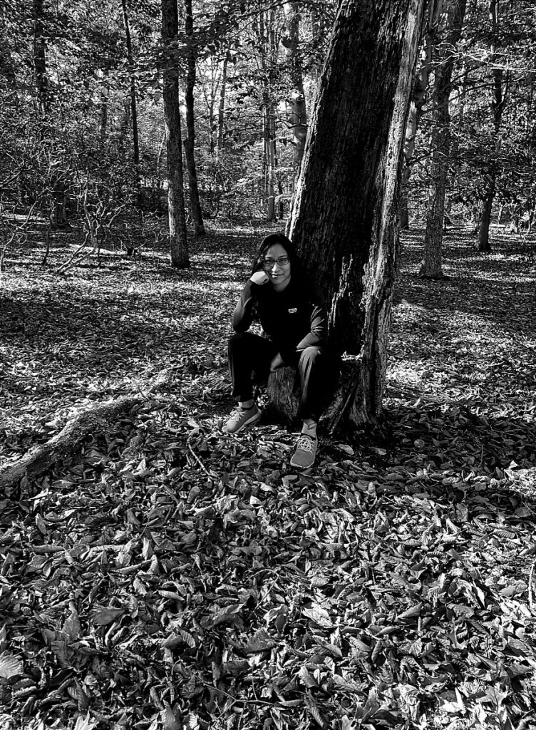 A woman in the forest sitting on the ground on the leaves leaning on a tall tree, black and white photo on the Journeyofsmiley blog