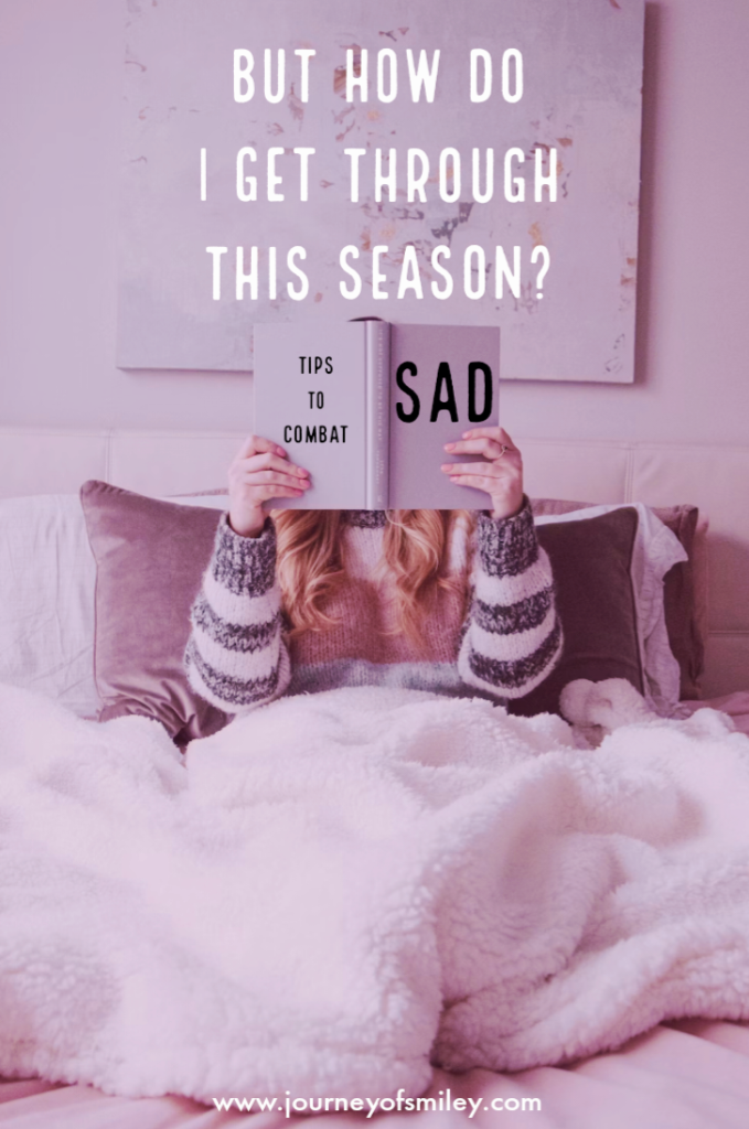 A woman in bed with a blanked on her legs reading a book with the title Tips to Combat SAD and over her head is hanging a picture with the words But How Do I Get Through This Season? on the Journeyofsmiley blog
