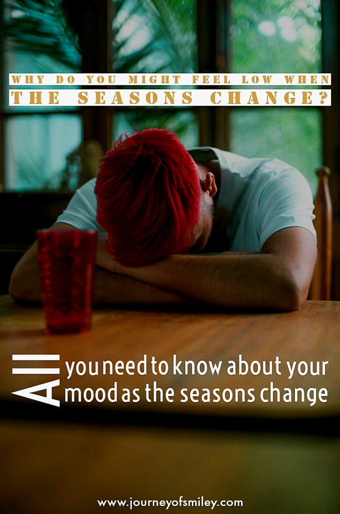 A man with red hair sitting at a table with his head down on his arms and the title is Why do you might feel low when the seasons change? All you need to know about your mood as the seasons change on the journeyofsmiley blog