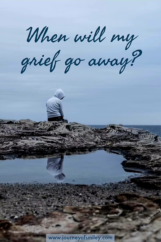 A person sitting on a rock with their face back looking towards the sea and behind them is a paddle. The title is When will my grief go away? on Journeyofsmiley.com