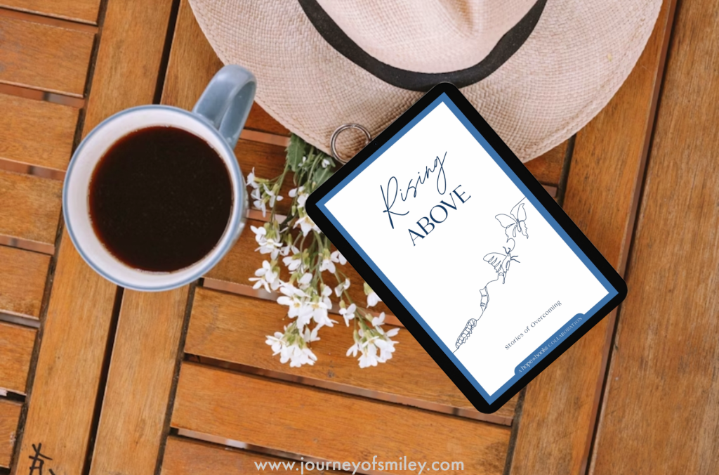 On a table is a cup of coffee, a hut, flowers and a book with the title Rising Above on Journeyofsmiley blog